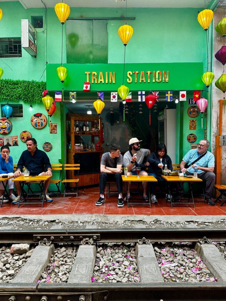 Touristen sitzen in einem Café direkt an den Gleisen der Hanoi Train Street und warten auf den vorbeifahrenden Zug, Hanoi Vietnam
