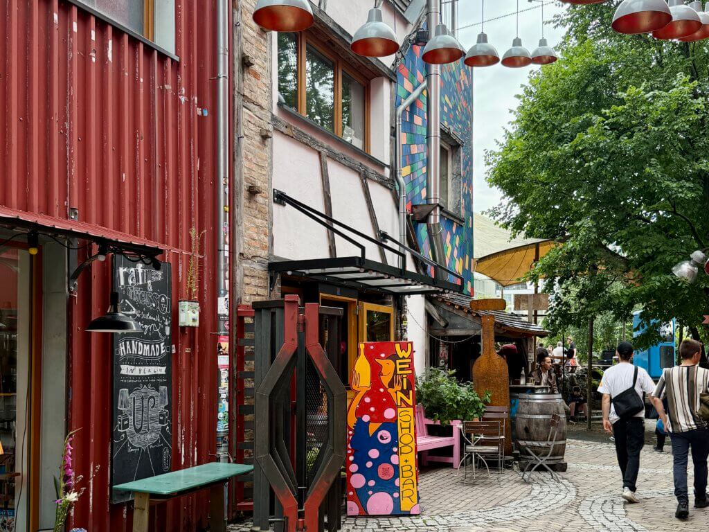 Straßenszene im Berliner Holzmarkt mit bunter Architektur, Weinbar, Werkstätten und flanierenden Besuchern – alternative Kultur am Spreeufer