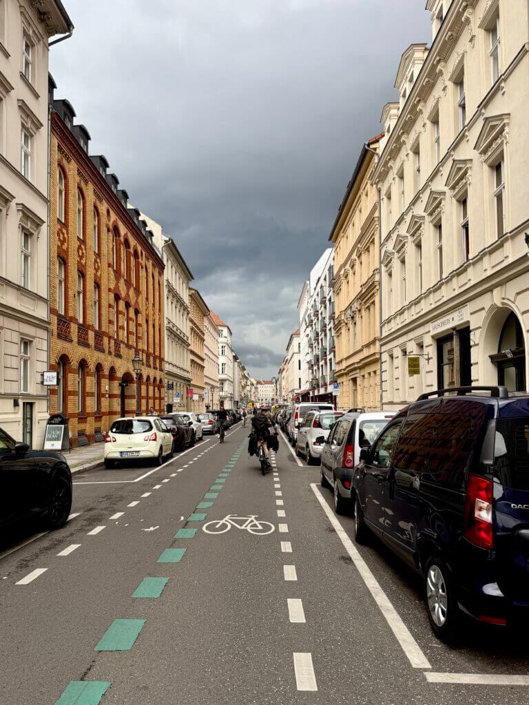 Linienstraße in Berlin‑Mitte mit Fahrradweg, historischen Fassaden und dramatischem Wolkenhimmel kurz vor Regen
