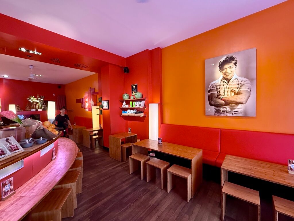 Innenansicht des vietnamesischen Restaurants Monsieur Vuong in Berlin mit roten Wänden, minimalistischen Holzmöbeln und Vintage-Porträt an der Wand