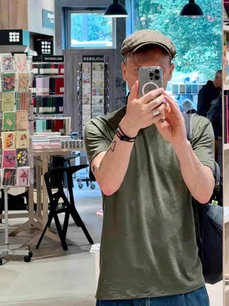 Berlin bei Regen: Person mit Kappe macht ein Selfie im Spiegel der Ocelot-Buchhandlung in Berlin-Mitte. Im Hintergrund: Bücherregale und ein urbanes, modernes Interior