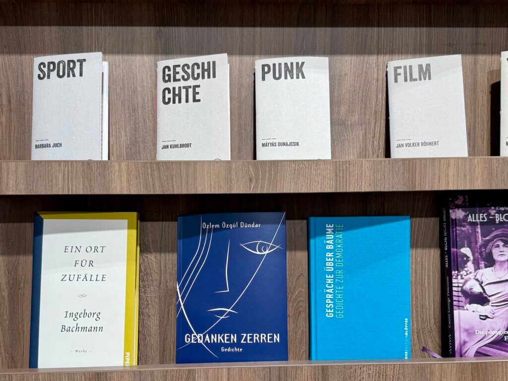 Innenansicht der Ocelot-Buchhandlung mit Leseplätzen vor großen Fenstern, Moleskine-Display und Menschen beim Schmökern in Berlin-Mitte