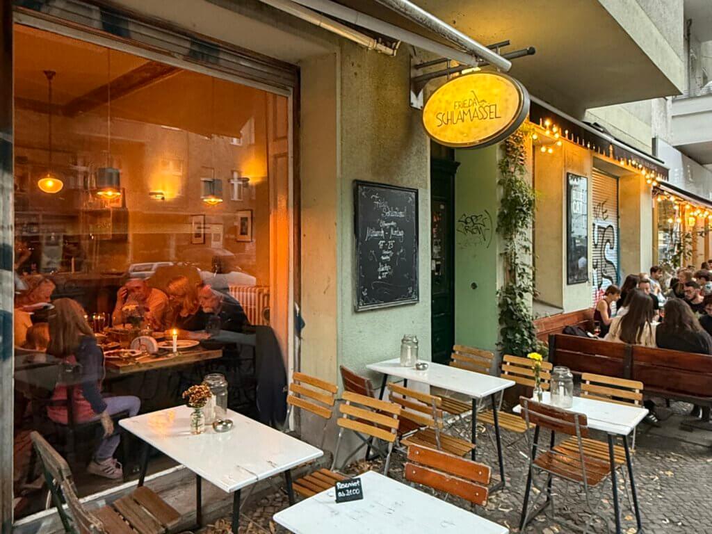 Außenbereich des Restaurants Frieda Schlamassel in Berlin, mit Tischen, Lichterkette und Gästen bei Abendessen.
