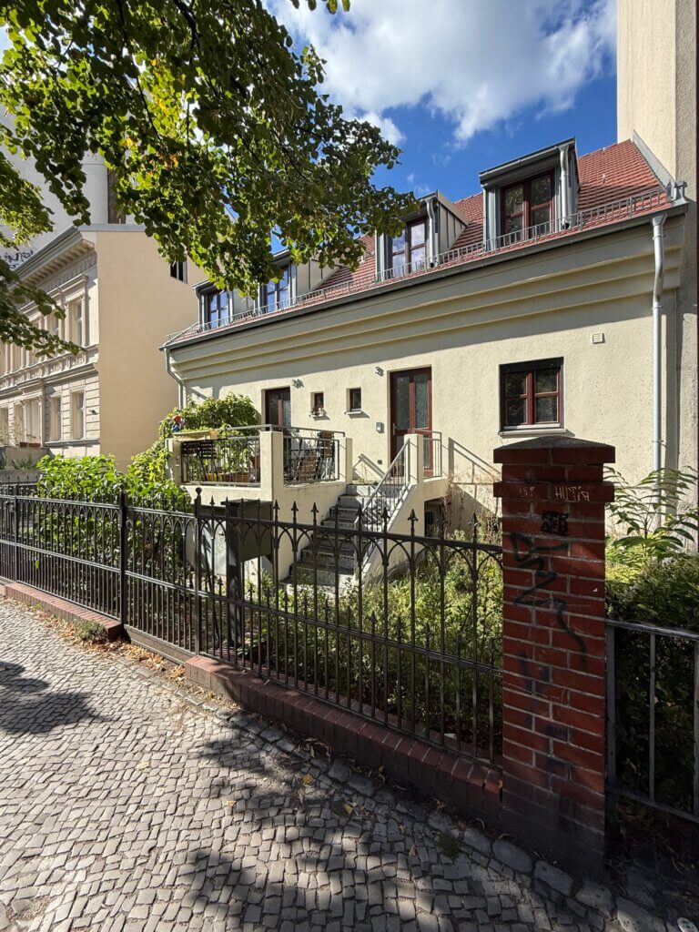 Ruhige Wohnstraße in Berlin-Rixdorf mit altem Kopfsteinpflaster, Zaun und niedrigen Altbauten mit Dachgauben.