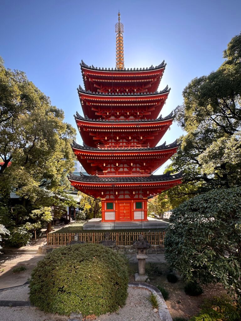 Fünfstöckige rote Pagode im Tocho-ji Tempel in Fukuoka, umgeben von Bäumen bei blauem Himmel.