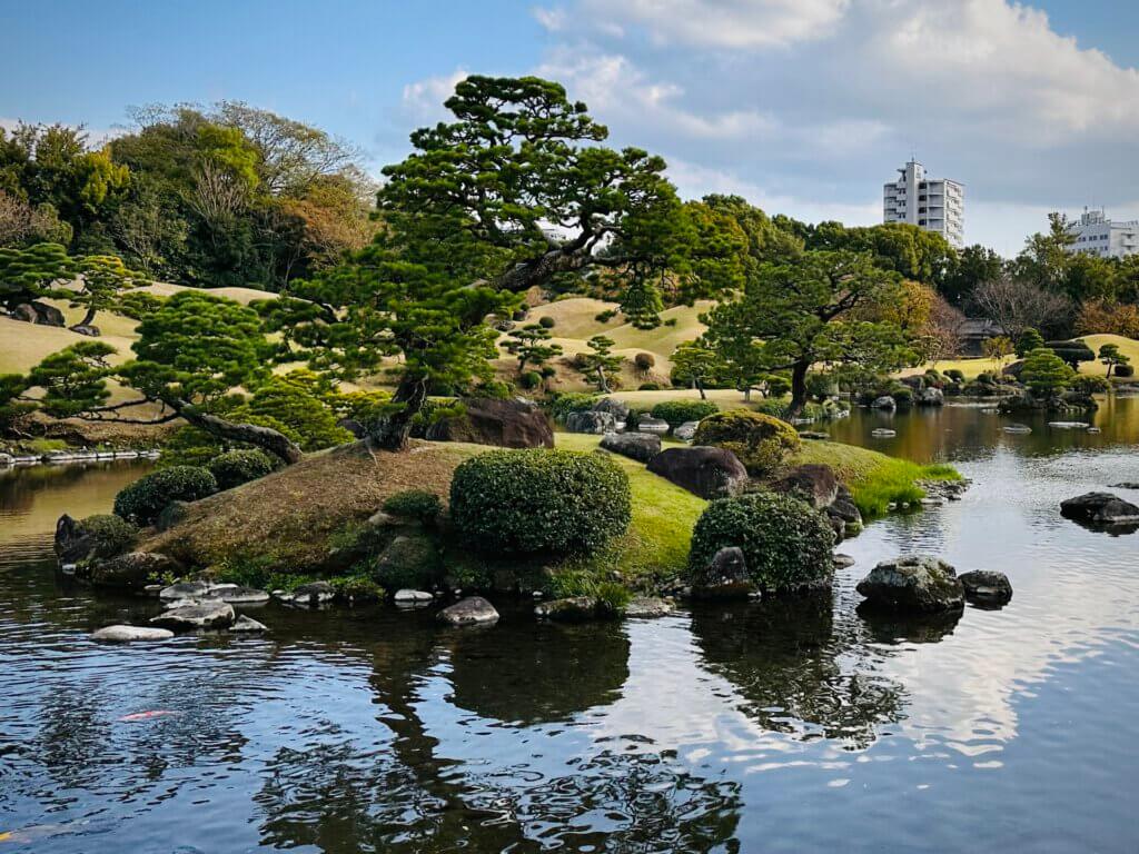 Japanischer Garten mit Teich, kleinen Inseln und kunstvoll geschnittenen Bäumen im Suizenji Jojuen Garden in Kumamoto.
