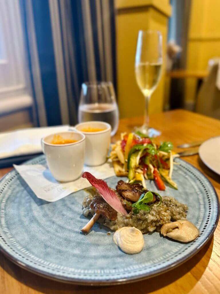 Gourmetgericht mit Pilzrisotto, Gemüsebeilage und Sektglas auf Holzplatte in einem Restaurant in Neuseeland