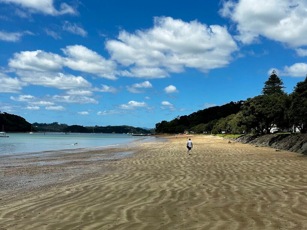 Einsamer Spaziergänger am goldenen Sandstrand von Paihia, Bay of Islands, bei leicht bewölktem Himmel